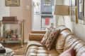 Living room with tan leather sofa, colorful pillows, bar cart, and view into kitchen with patterned tiles and globe decor.