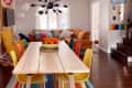 Overview of dining room and living area with black starburst chandelier, black and white polka dot wallpaper, and orange leather sectional, and yellow lounge chair