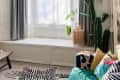 Cozy living room with a green sofa, zebra rug, large plants, and a wicker chair by a bay window.