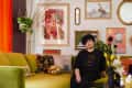 Woman sitting on a green sofa in a colorful living room with eclectic wall art and vibrant decor.