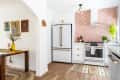 Bright kitchen with floral wallpaper, white cabinets, retro fridge, and a wooden table with a yellow vase and artwork.
