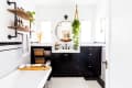 Bathroom with black vanity, round mirror, hanging plant, wooden shelves, and a bathtub with a tray holding towels and candles.