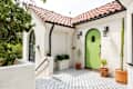 Spanish-style entryway with a green arched door, terracotta roof, potted plants, and patterned tile floor.