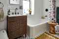Modern bathroom featuring a wooden vanity with a white sink, colorful shower curtain, and a round wooden side table.