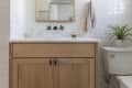 Bathroom with wooden vanity, white subway tiles, round mirror, brass sconces, and a potted plant on the toilet.
