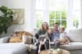 Family sitting on a light gray sofa with two dogs, surrounded by modern decor and large windows.