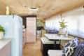 Retro-style kitchen in a converted bus with a pastel blue fridge, potted plants, and a dining area with patterned cushions.