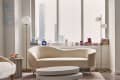 Modern living room with cream sofas, round coffee table, floor lamps, books, and "Cloud 9" neon sign on the wall.