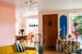 Colorful living room with yellow sofa, striped pillow, glass chandelier, and dining area with wooden table and chairs.