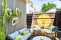 Outdoor patio with wicker chairs, blue cushions, a blue sofa, and wall planters. Yellow circle decor on wooden fence.
