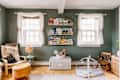 Children's room with green walls, bookshelves, wicker chair, play mat, and wooden rocking chair.