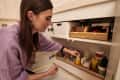 Woman organizing bathroom cabinet with labeled wooden bins and various toiletries.