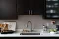 Modern kitchen with dark cabinets, stainless steel faucet, artichokes in a bowl, and wooden utensils on a white countertop.