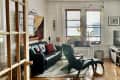 Living room with black leather sofa, green armchair, abstract art, plants, and a TV on a wooden stand.