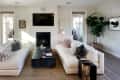 Two cream sofas facing each other in a living room with a black marble coffee table, wall-mounted TV, and large potted plant.