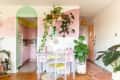 Pastel-themed kitchen and workspace with pink cabinets, green plants, and a lavender desk under a shelf with hanging vines.