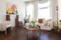 Living room with white sofa, colorful cushions, wooden floor, abstract art, plants, and a round coffee table with decor.