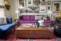 Eclectic living room with purple sofa, colorful wall art, patterned coffee table, and blue chair on a vibrant rug.