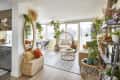 Bright living room with wicker furniture, large mirror, plants, and city view through windows.