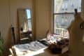 Sewing room with mannequin, fabric, yarn, iron, and a guitar by a window with a view of a building and fire escape.