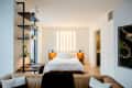 Modern bedroom with a white bed, wooden nightstands, vertical light fixture, and black shelving with plants.