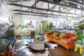 Loft-style living room with orange sofa, colorful pillows, glass coffee table, plants, and exposed beams.