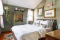 Cozy bedroom with green walls, white bedding, hanging plant, and framed art.