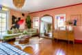 Living room with green velvet sectional, large mirror, wooden dresser, abstract wall art, and colorful stained glass windows.