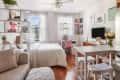 Cozy studio apartment with a bed, sofa, white shelves, pink chair, and wall art, featuring a TV and a small dining area.