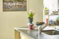 Kitchen with gray countertop, vase of pink tulips, fruit bowl, and colorful wall art under yellow pendant lights.