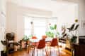 Dining room with orange chairs, white table, large windows, and various potted plants.