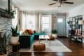 Living room with teal sectional sofa, colorful cushions, poufs, plants, and a light blue door.