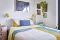 Colorful bedroom with a patchwork quilt, yellow lamps, wall art, and hanging plant.