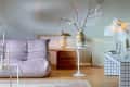 Lavender sofa, round table with vase and branches, gold lamp, and modern lighting in a stylish living room.
