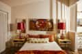 Bedroom with red lamps, abstract tree artwork, yellow nightstands, and a bed with orange and white pillows.