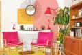 Colorful living room with pink cushioned chairs, a sunburst mirror, red lamp, and a large plant near a wooden cabinet.