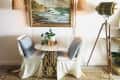 Dining area with small table and two chairs below a painting of the sea