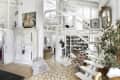 Open-plan living area with white staircase, vintage armoire, colorful armchair, and bookshelves, featuring eclectic decor.