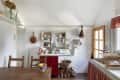 Rustic kitchen with red cabinets, open shelves, wooden table, and a bowl of lemons. Logs and wicker basket under counter.
