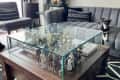 Glass-top coffee table with action figures, gray sofa, black and white rug, and a small dog sitting on the sofa.