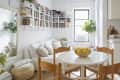Cozy kitchen and living area with a round table, wooden chairs, bowl of lemons, white sofa, and wall-mounted bookshelves.