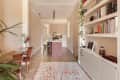 Open kitchen with pink island, bar stools, herringbone floor, bookshelves, and a colorful rug.