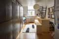 Wide angle of a small studio apartment with a long wall of black storage cabinets to the left and a natural wood dining table and bench