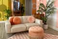 Retro living room with cream sofa, orange and pink pillows, peach ottoman, and vibrant yellow and pink walls with geometric patterns.