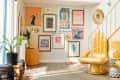 Eclectic living room with gold hand chairs, vibrant art gallery wall, and a small orange lamp on a patterned side table.