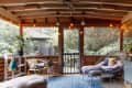 Cozy sunroom with wicker chair, potted plants, string lights, and a blue patterned rug.