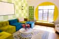Living room with green and yellow checkered walls, colorful modular sofa, round window, and floral centerpiece on a coffee table.