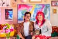 Couple sitting on a sofa with a cat, surrounded by colorful art and decor, including vibrant pillows and flowers.