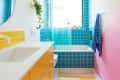 Brightly colored bathroom featuring yellow tiled vanity, turquoise wall tiles, a white bathtub, and a pink accent wall.