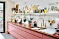 Modern kitchen with pink cabinetry, wooden countertop, brass faucet, and decorative items on shelves.